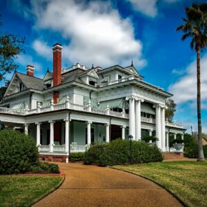 Beautiful white mansion with pillars and palm trees under a bright blue sky.